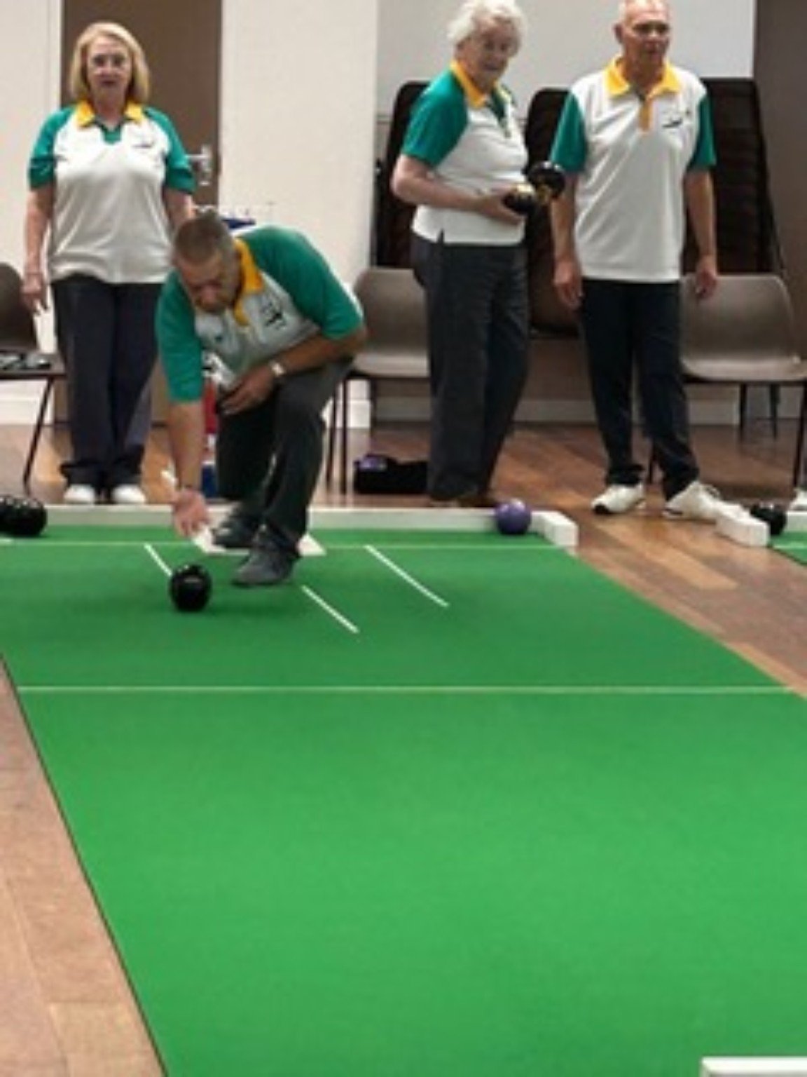A Woodhall Spa Short Mat Bowls Club member bowling while fellow members watch