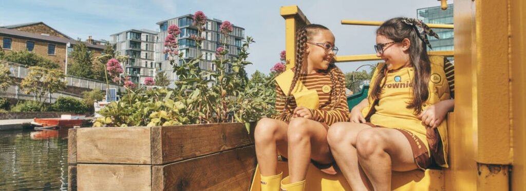 Two Brownies in uniform sitting together outdoors; representative Girlguiding photograph