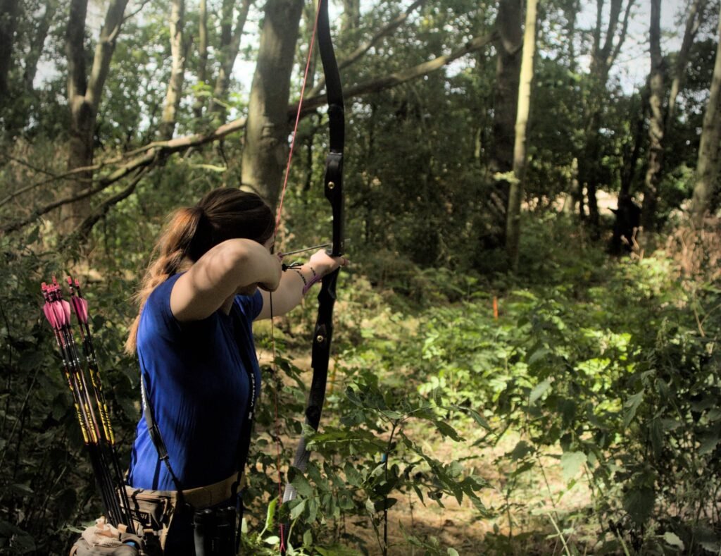 Archer aiming a bow in woodland at Castle Bowmen Archery Club
