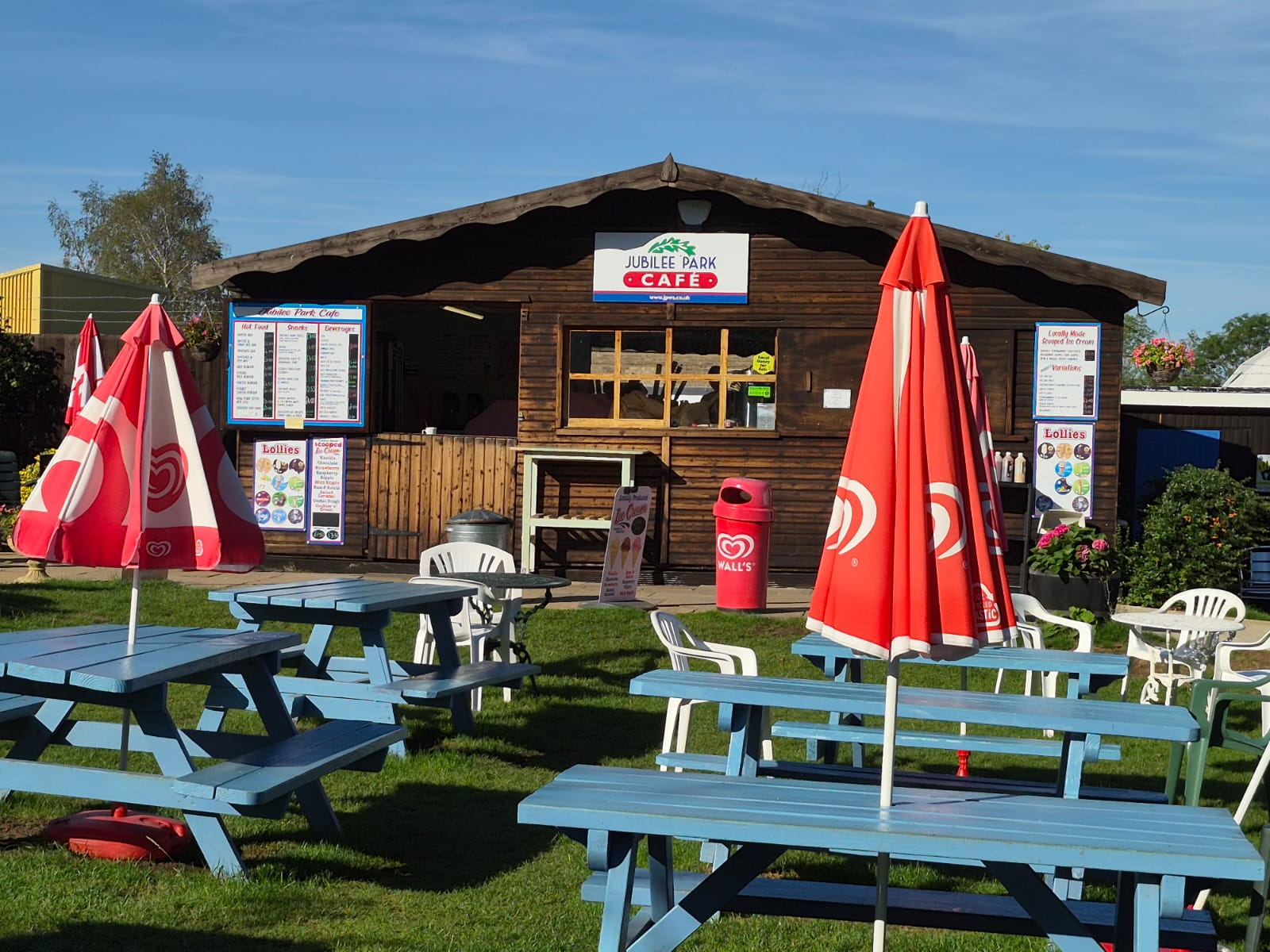 Blue picnic tables and red parasols outside Jubilee Park Café