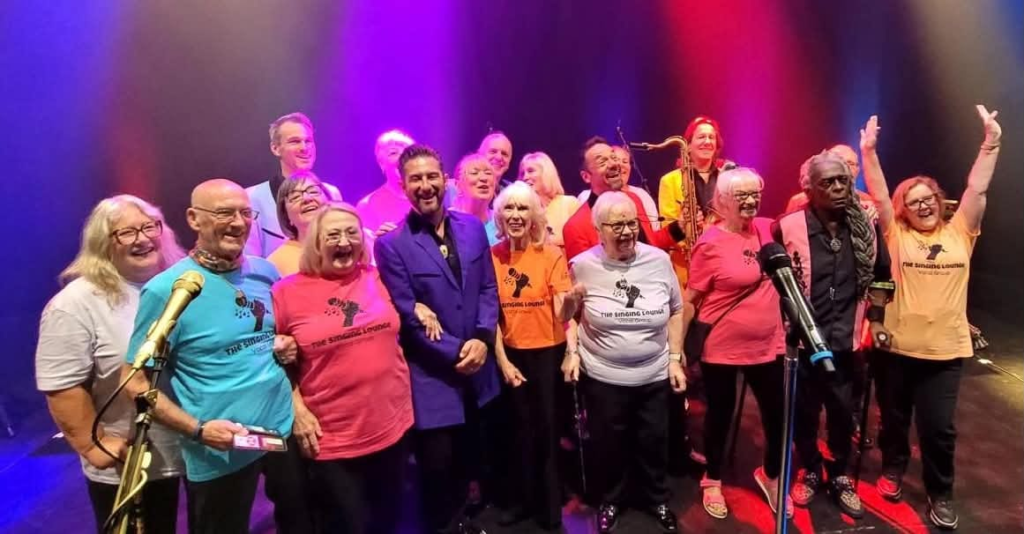 The Singing Lounge group together on stage in colourful T-shirts.