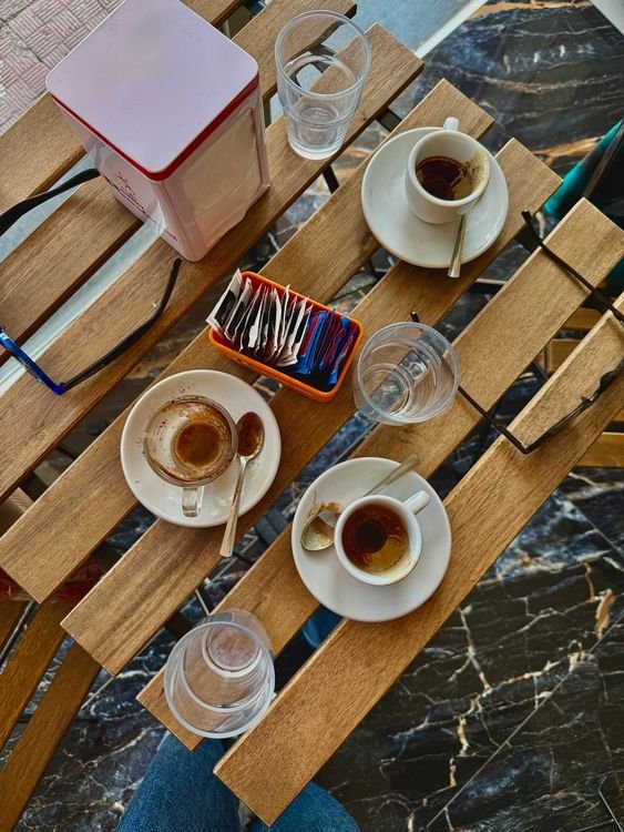 Coffee cups and water glasses on a wooden cafe table; representative photograph