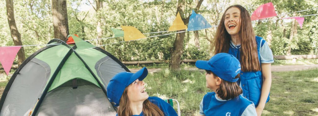 Guides in blue uniforms beside a tent outdoors; representative Girlguiding photograph