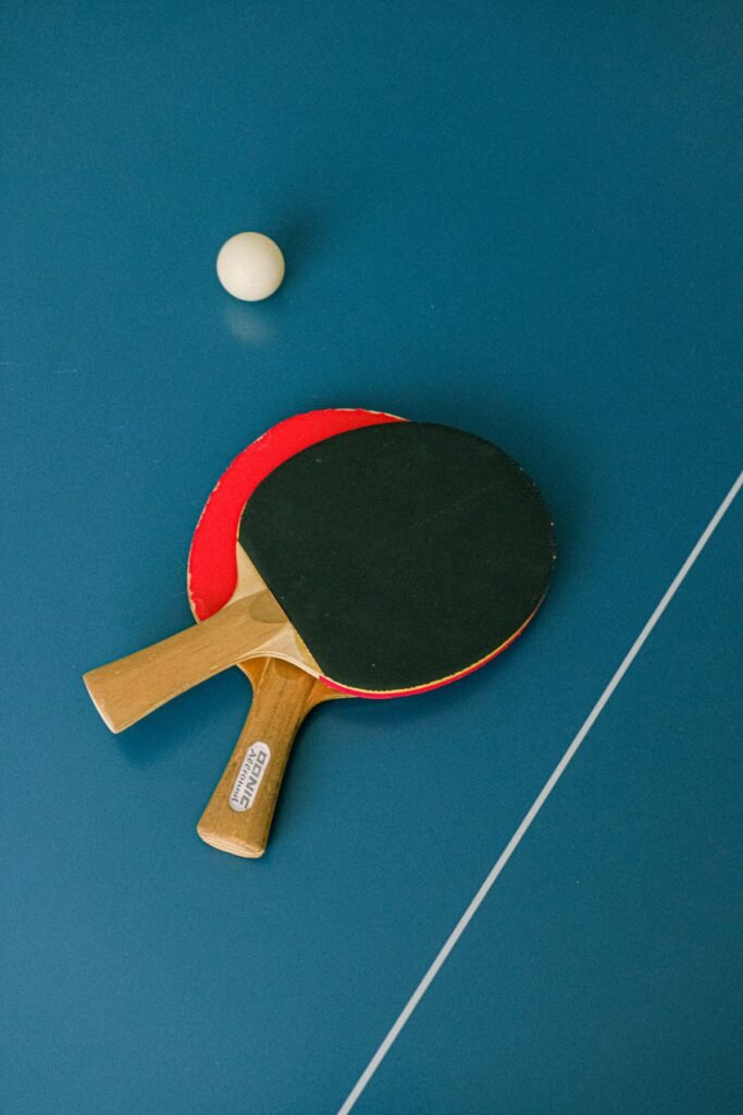 Red and black table tennis bats with a white ball on a blue table; representative sport photograph
